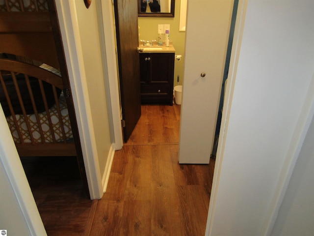 hallway featuring a sink, baseboards, and wood finished floors