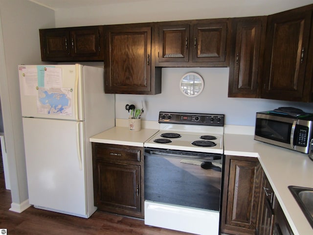 kitchen featuring white appliances, dark wood finished floors, a sink, light countertops, and dark brown cabinetry