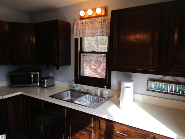 kitchen with dark brown cabinetry, stainless steel microwave, light countertops, and a sink