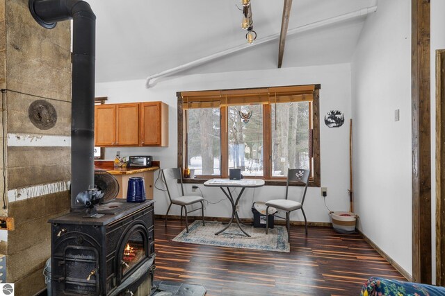 dining space with baseboards, dark wood finished floors, a wood stove, and vaulted ceiling