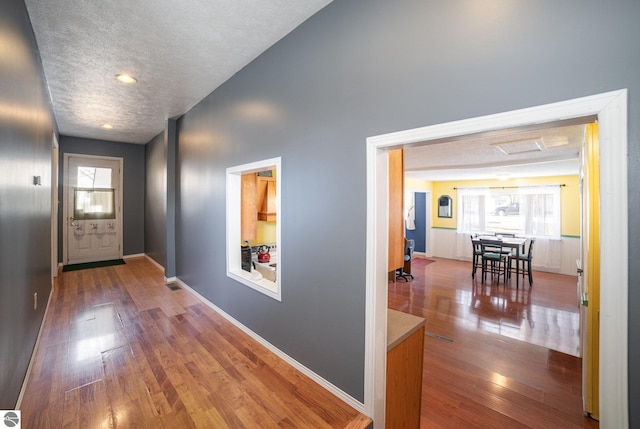 hallway featuring visible vents, a textured ceiling, baseboards, and wood finished floors