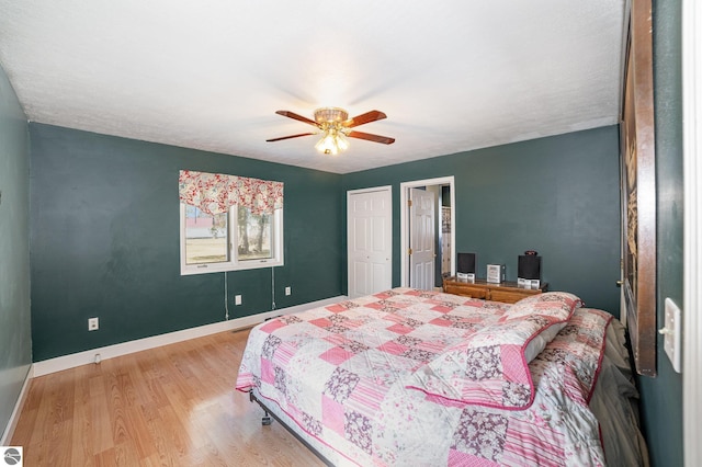bedroom with ceiling fan, baseboards, wood finished floors, and multiple closets