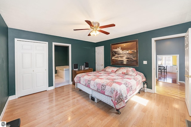 bedroom with two closets, baseboards, light wood-style flooring, ensuite bathroom, and a ceiling fan