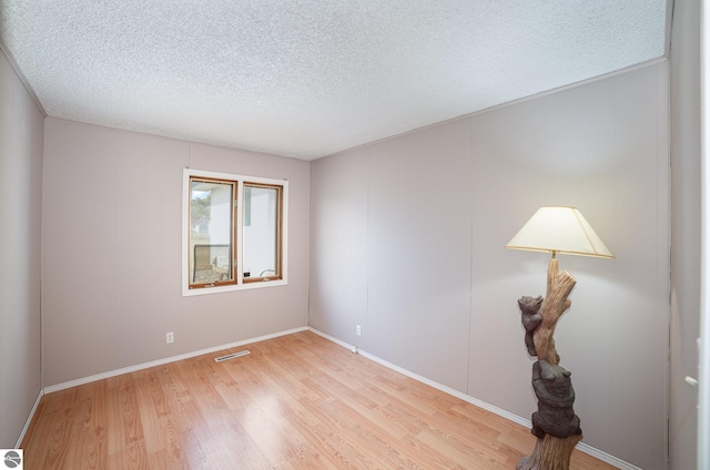 unfurnished room featuring baseboards, light wood-style floors, visible vents, and a textured ceiling