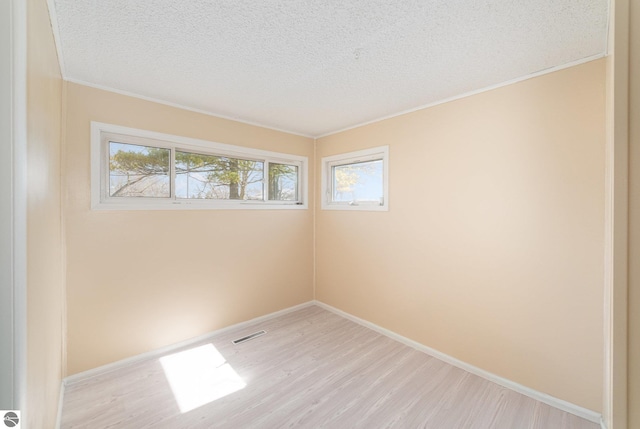 empty room featuring visible vents, a textured ceiling, light wood-type flooring, and baseboards