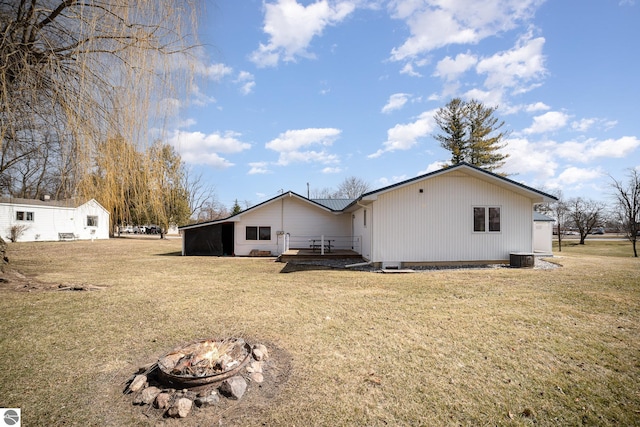 rear view of property with a wooden deck, a lawn, and a fire pit