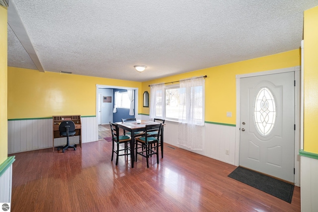 dining area featuring a textured ceiling, wood finished floors, and wainscoting