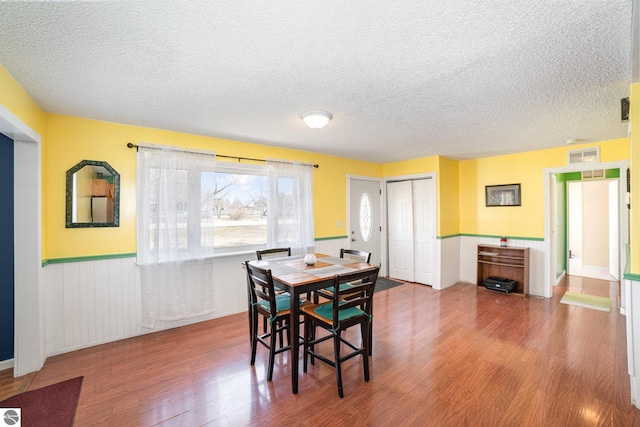 dining space featuring a wainscoted wall, a textured ceiling, visible vents, and wood finished floors