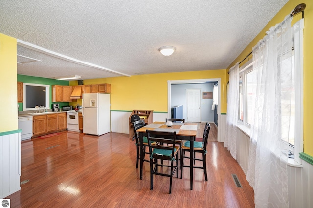 dining room featuring a wainscoted wall, wood finished floors, visible vents, and a textured ceiling