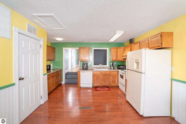 kitchen featuring a sink, visible vents, white appliances, and wood finished floors