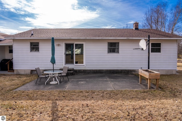 back of house featuring a patio, a lawn, roof with shingles, and a chimney