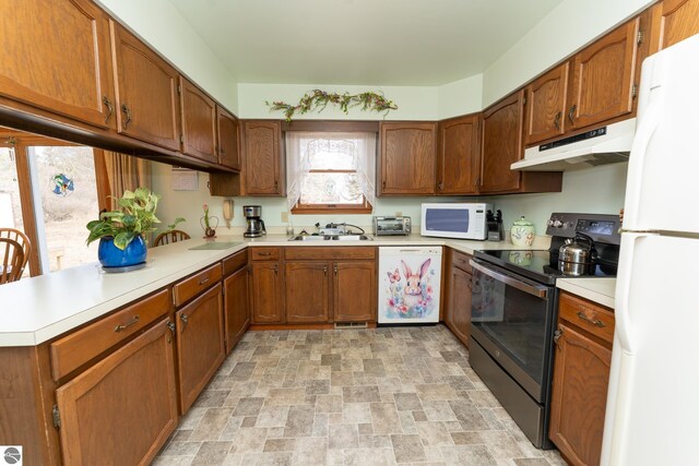 kitchen featuring under cabinet range hood, light countertops, brown cabinetry, stone finish floor, and white appliances