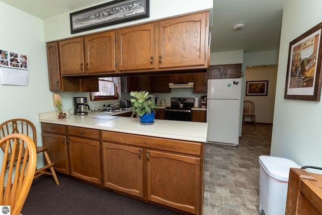 kitchen featuring a peninsula, freestanding refrigerator, electric range oven, light countertops, and stone finish floor