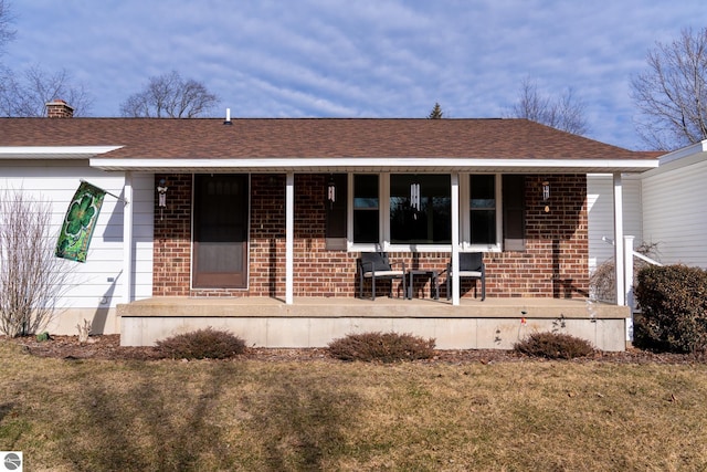 view of front of property featuring brick siding, covered porch, a front yard, and roof with shingles