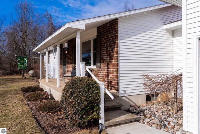 view of exterior entry featuring brick siding and a porch