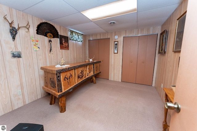 interior space featuring wooden walls, carpet, visible vents, and a paneled ceiling