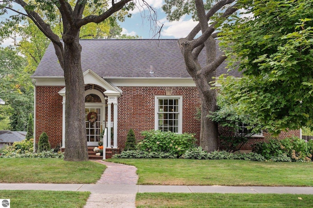 view of front of home with a front lawn, brick siding, and a shingled roof