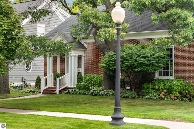 view of front of home with brick siding, a front yard, and roof with shingles