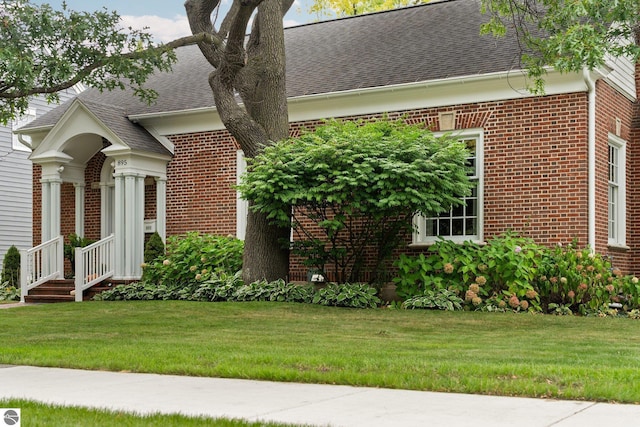 view of front facade featuring brick siding, a front lawn, and roof with shingles