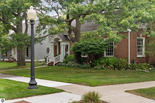 view of front of home with a front yard, brick siding, and a shingled roof