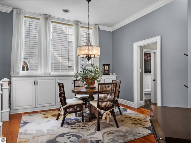 dining space with baseboards, wood finished floors, visible vents, and ornamental molding