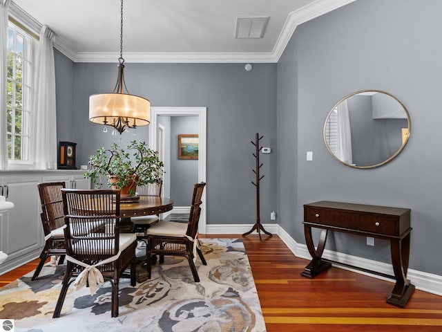 dining space featuring visible vents, crown molding, baseboards, and wood finished floors