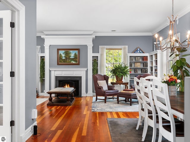 dining area with a fireplace with flush hearth, an inviting chandelier, wood-type flooring, and crown molding