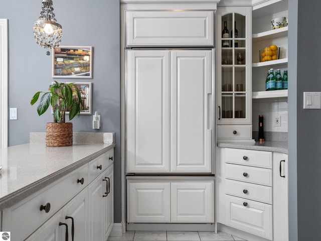 kitchen featuring hanging light fixtures, white cabinetry, glass insert cabinets, and light stone counters