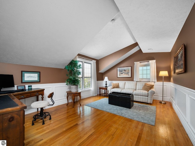 interior space featuring vaulted ceiling, light wood-style floors, wainscoting, and a textured ceiling