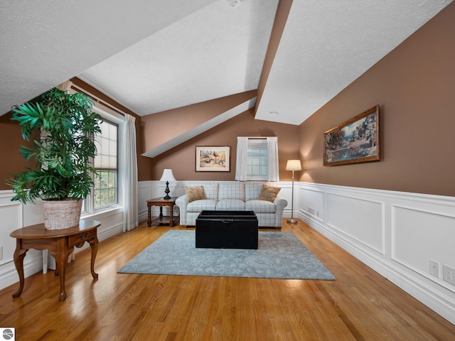 living area featuring a textured ceiling, wainscoting, vaulted ceiling with beams, and light wood finished floors