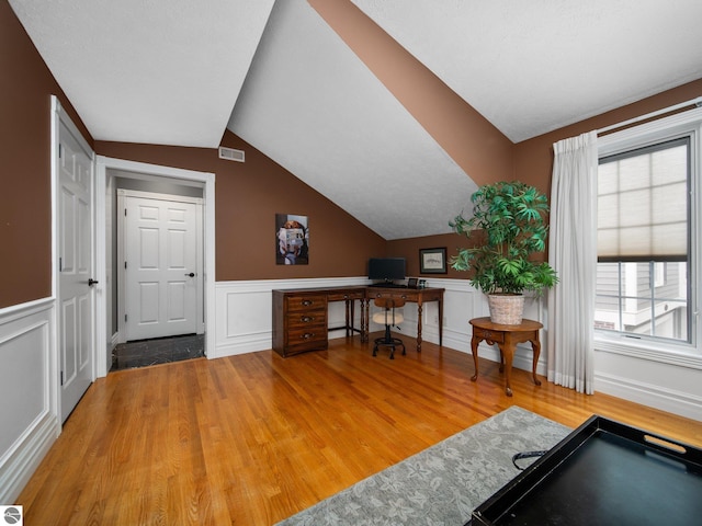 office featuring light wood-type flooring, visible vents, wainscoting, and vaulted ceiling