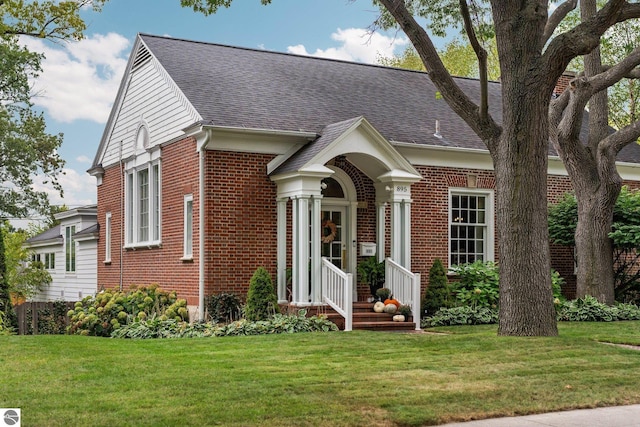 view of front facade with brick siding, a shingled roof, and a front yard