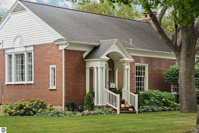 view of front facade with a front yard, brick siding, and a chimney