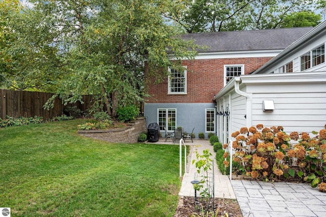 rear view of house with a yard, a patio, brick siding, and fence