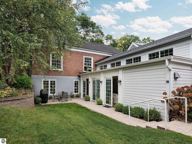 rear view of property featuring a patio area, a lawn, and brick siding