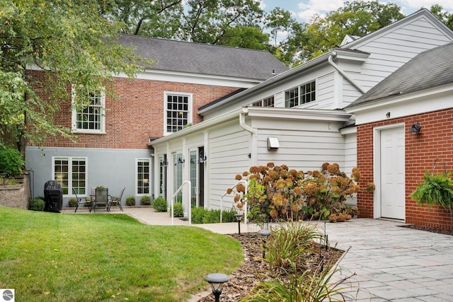 rear view of house with a patio, a yard, and brick siding