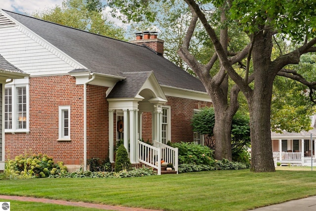 exterior space featuring brick siding, a chimney, a yard, and a shingled roof