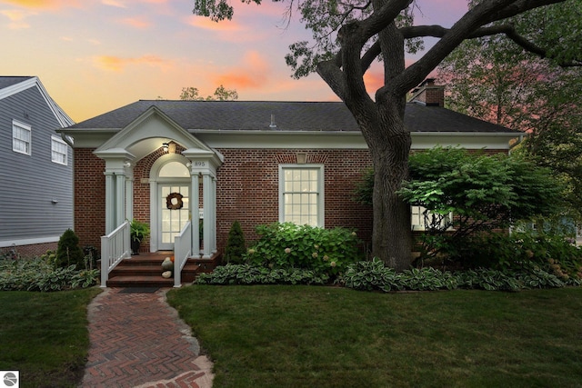 view of front of home with a front yard, brick siding, and a chimney