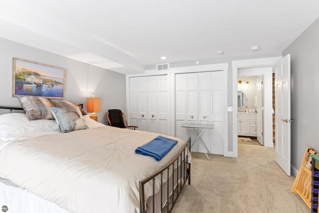 bedroom featuring visible vents, light carpet, two closets, recessed lighting, and connected bathroom