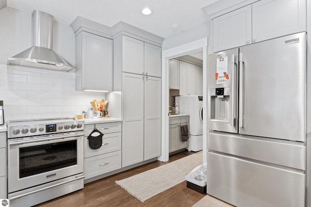 kitchen with tasteful backsplash, wood finished floors, appliances with stainless steel finishes, wall chimney exhaust hood, and light countertops