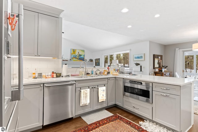 kitchen featuring built in microwave, dishwasher, light countertops, a peninsula, and a sink