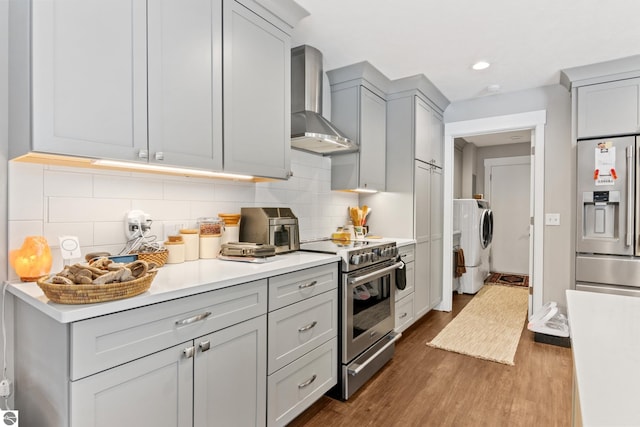 kitchen featuring wall chimney range hood, dark wood-style floors, stainless steel appliances, separate washer and dryer, and light countertops