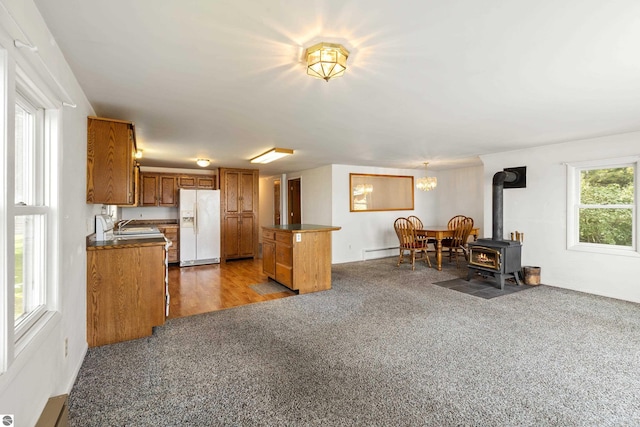 kitchen with dark countertops, brown cabinets, a wood stove, white fridge with ice dispenser, and a baseboard radiator