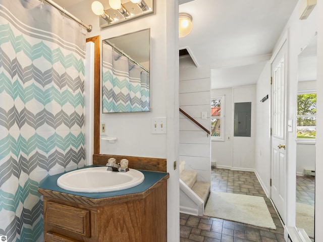 full bath with vanity, electric panel, baseboards, and stone tile flooring