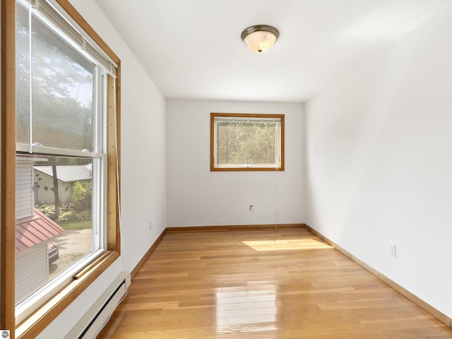 unfurnished room with baseboard heating, baseboards, and light wood-style floors