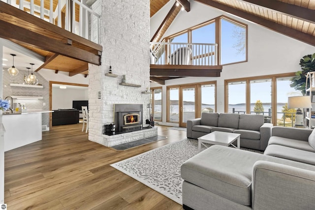 living room with beamed ceiling, plenty of natural light, a stone fireplace, and wood finished floors