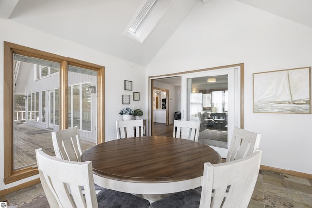 dining space with a skylight, baseboards, high vaulted ceiling, and stone tile flooring