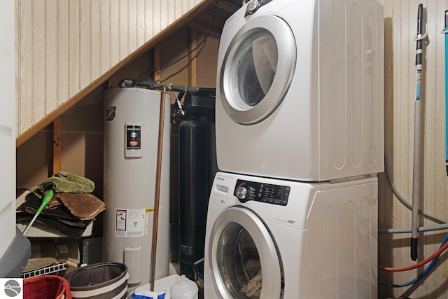 clothes washing area featuring laundry area, stacked washer and dryer, and water heater