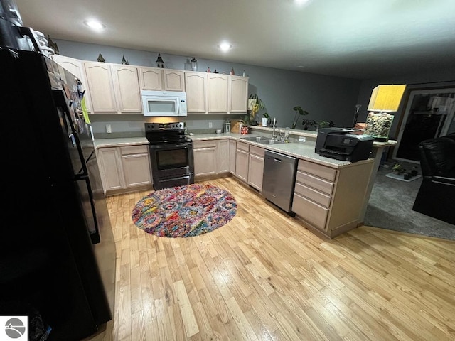 kitchen with black appliances, light countertops, light wood-type flooring, and a sink