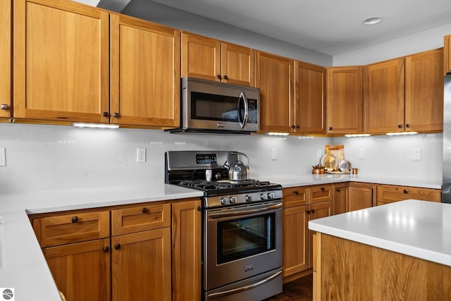 kitchen featuring stainless steel appliances, brown cabinetry, and light countertops